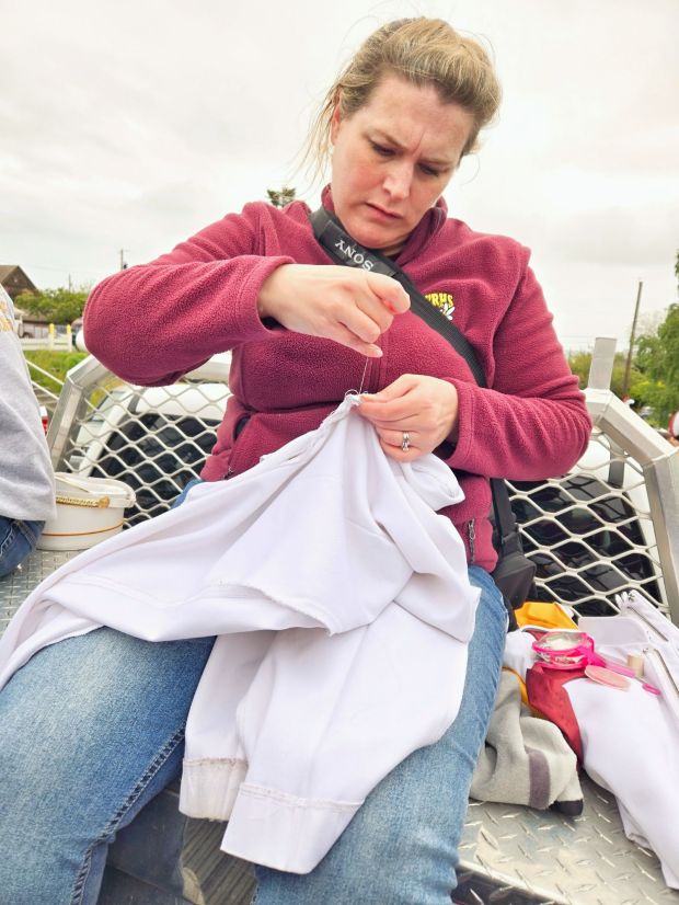 Band Mom mends a pair of drum major pants in the back of a truck en route to a parade