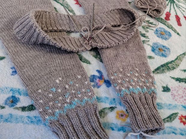 Sleeves and bottom ribbing of a handknit yoked colorwork sweater, made with gray, aqua, and white yarn.