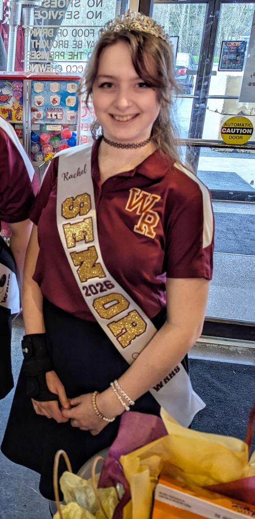 A senior high school girl wearing a personalized Class of 2026 senior sash with gold and maroon letters