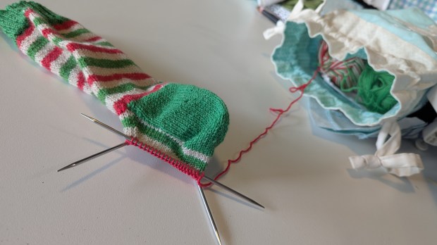 Handknit sock in-progress in red, white, and green self-striping yarn