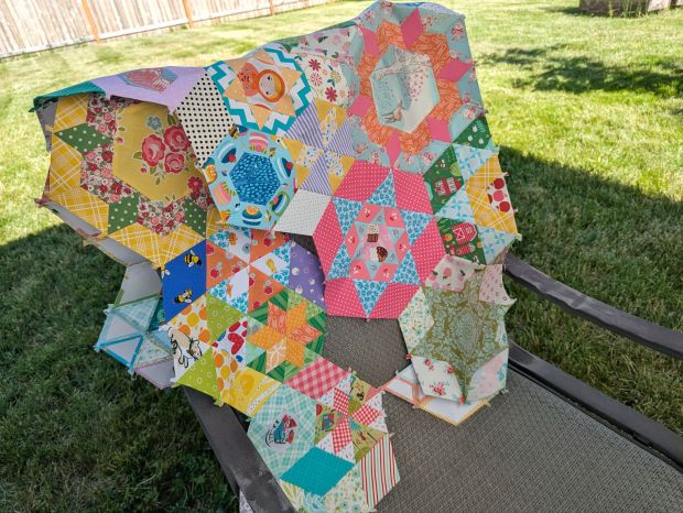 In-progress shot of a scrappy "Smitten" English paper pieced quilt in a rainbow of colors.