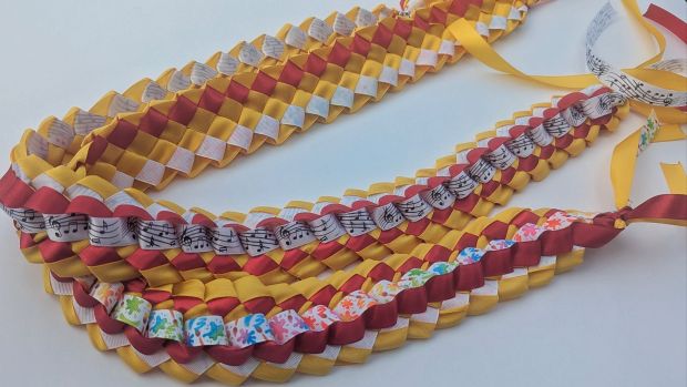 Music and artist ribbon graduation leis in maroon, gold, and white.