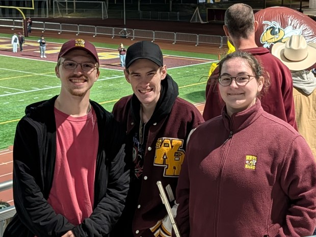 Three young adults pose together at their pep band alumni night.